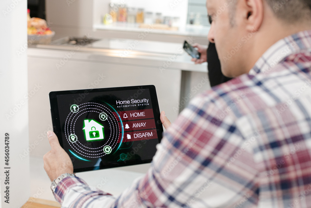 Obraz premium Man setting smart home alarm system from digital tablet on living room sofa
