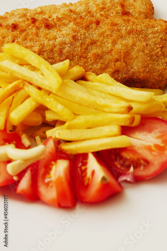 Traditional fish and chips on white plate with fresh cut tomatoes. Simple meal serving. Sea food.