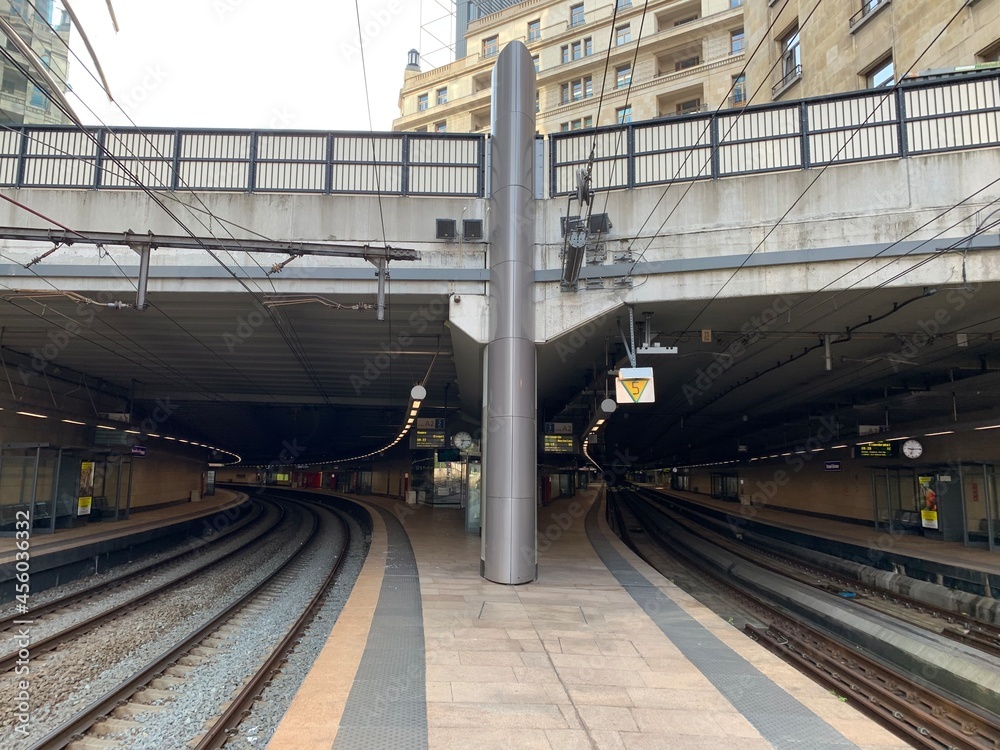 Fototapeta premium Entrance to the modern tunnel of underground Brussels Schuman train, railway station. Symetric tracks. European quarter buildings on top and around. Bruxelles, Brussels Capital region, Belgium.