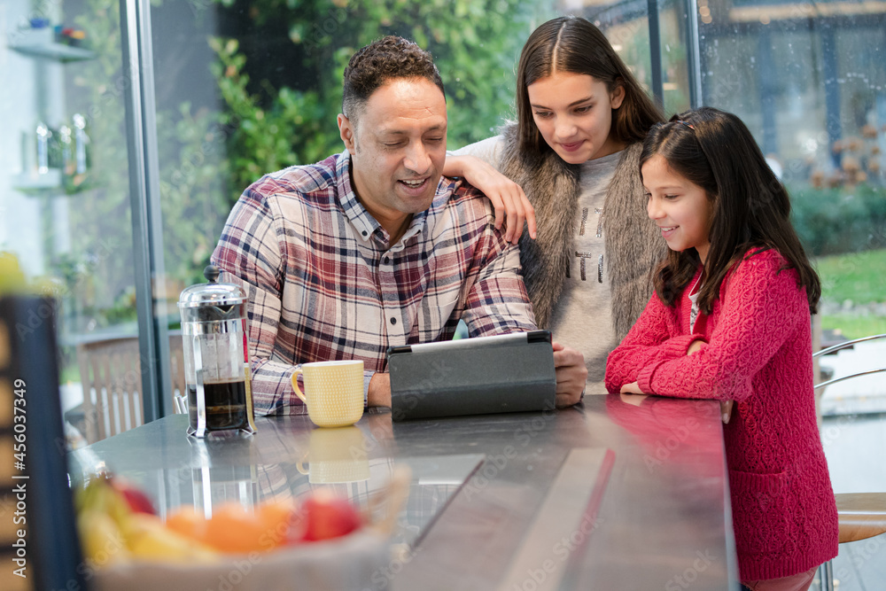 Father and daughters using digital tablet in morning kitchen Father and daughters using digital tablet in morning kitchen