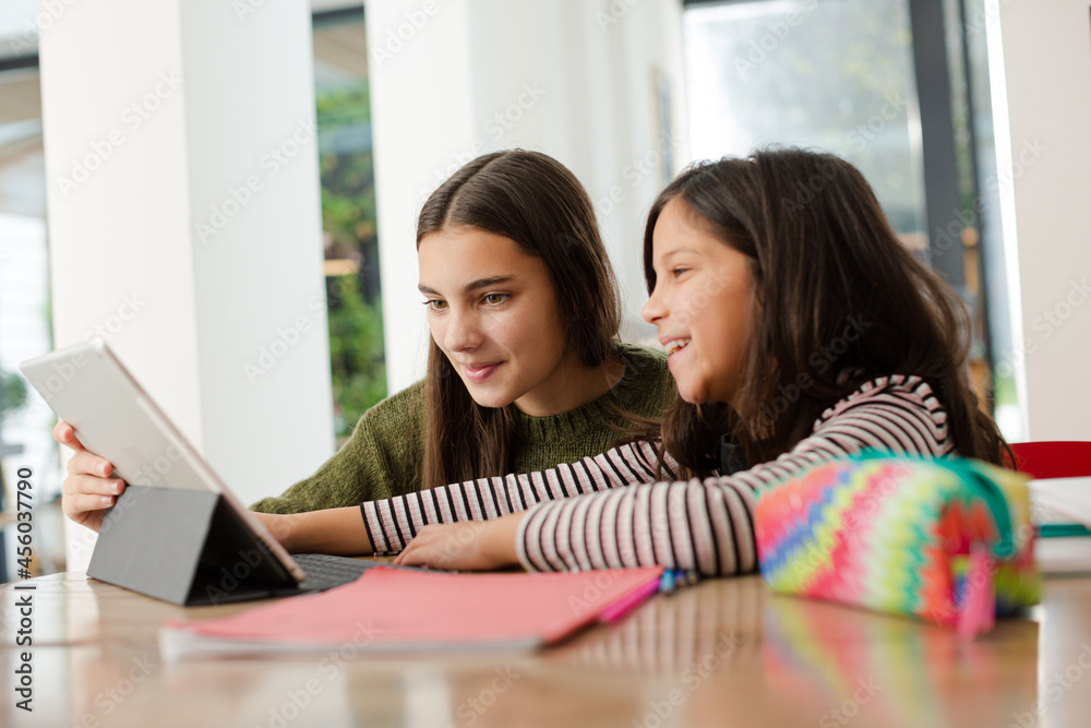 Obraz premium Sisters doing homework, sharing digital tablet at table