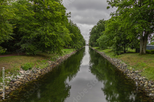 A narrow canal with paved banks. The canal is surrounded by large deciduous trees that are reflected in the water surface © Knut