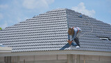 Workers are installing gray roof tiles wearing seat belts to ensure safe working at heights.