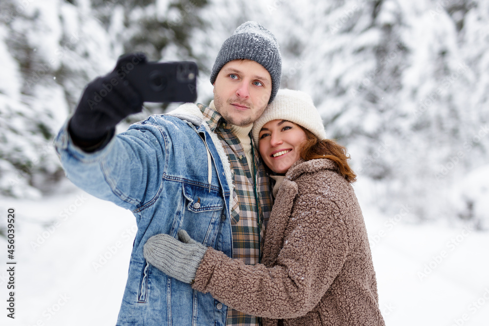 happy couple hugging and taking selfie photo in winter forest