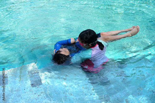 Two children play in the hotel pool on vacation, float in the water, teach swimming, siblings, shot by high-angle camera.