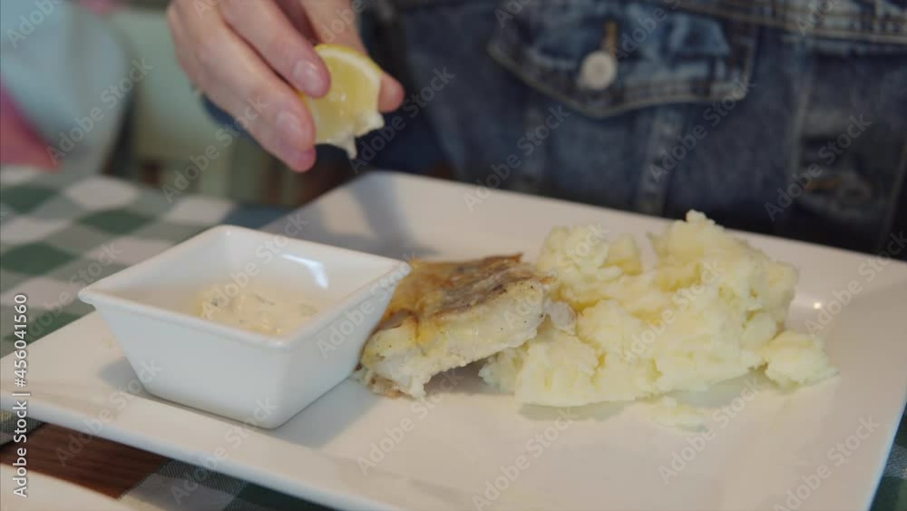 A girl in a denim jacket pours lemon juice on the fish. A girl in a denim jacket pours lemon juice on the fish.