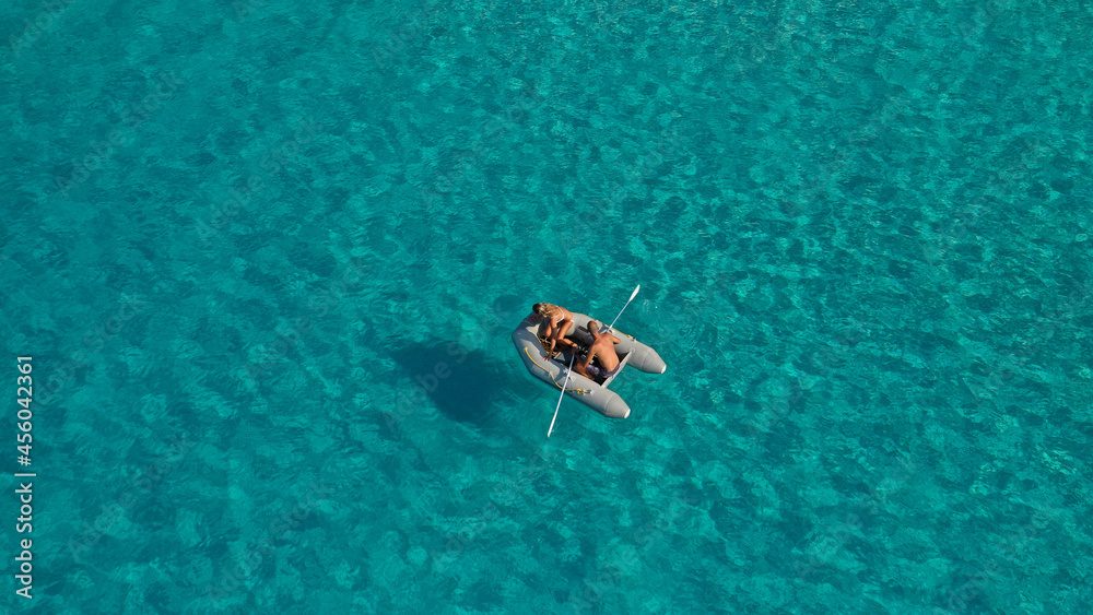 Aerial drone photo of small inflatable rib boat operated by young couple in turquoise clear water sea