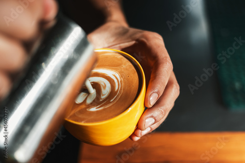 Closeup shot of brunette male hands holding a yellow cup and a steel jug preparing a latte.