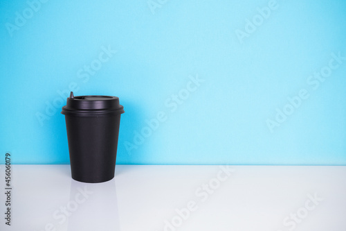 Black paper cup on white table and blue background