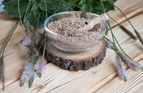 A close-up of the psyllium superfood in a transparent plate with a wooden spoon on a piece of wood . The concept of useful food additives.