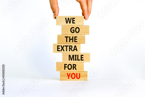 Go the extra mile symbol. Wooden blocks with words 'We go the extra mile for you'. Businessman hand. Beautiful white background. Business and go the extra mile concept. Copy space.