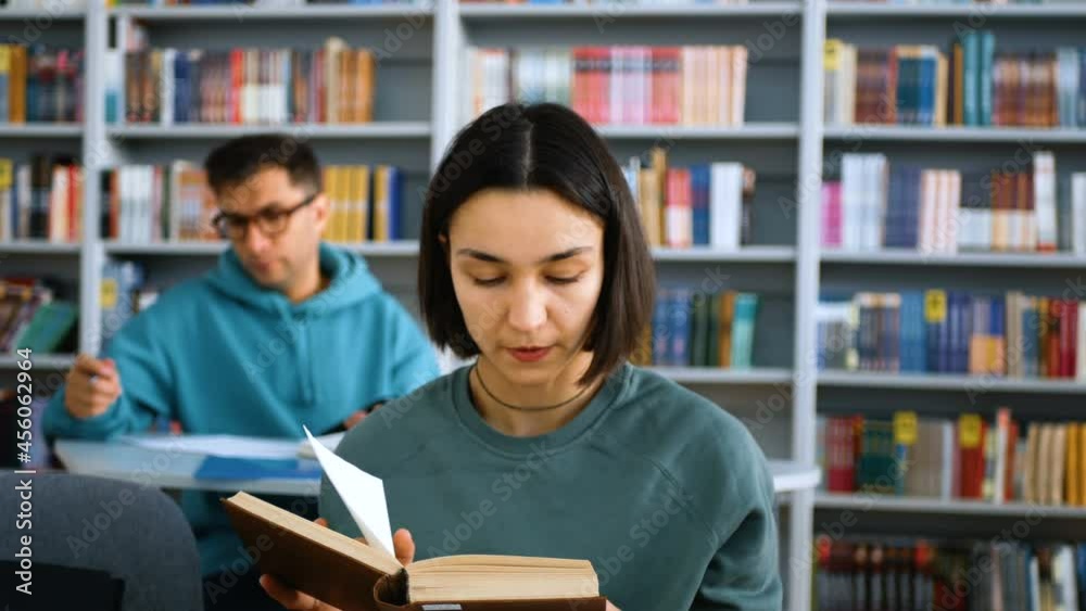 Young attractive university students are preparing for the test, they are sitting at the tables in the public library and writing the necessary information in notebooks.Close-up portrait of a young Young attractive university students are preparing for the test, they are sitting at the tables in the public library and writing the necessary information in notebooks.Close-up portrait of a young