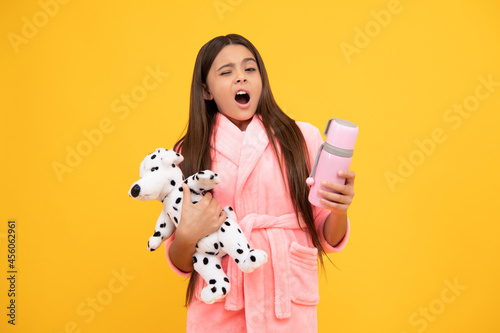 Fotografie yawning teen girl in home terry bathrobe with toy and thermos bottle, yawn