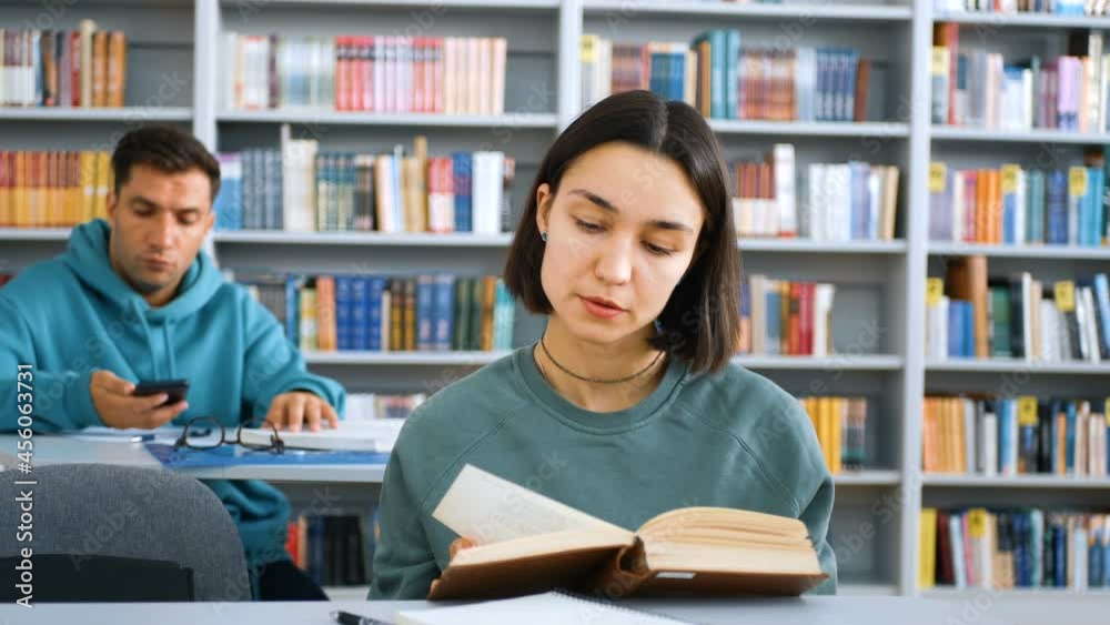 Young attractive university students are preparing for the test, they are sitting at the tables in the public library and writing the necessary information in notebooks. Education concept. Young attractive university students are preparing for the test, they are sitting at the tables in the public library and writing the necessary information in notebooks. Education concept.