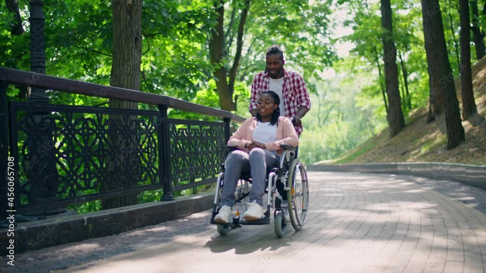 Male friend pushing young woman's wheelchair, life with disability, support Male friend pushing young woman's wheelchair, life with disability, support