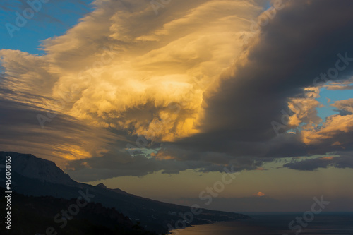 A thundercloud in the orange-beige sunset light. Dramatic stormy sky. A huge cumulus cloud in the form of a whirlpool. A harbinger of bad weather, climate change, a natural disaster. Before the rain © Anna Pismenskova