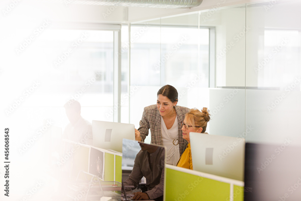 Businesswomen talking at computer in open plan office Businesswomen talking at computer in open plan office