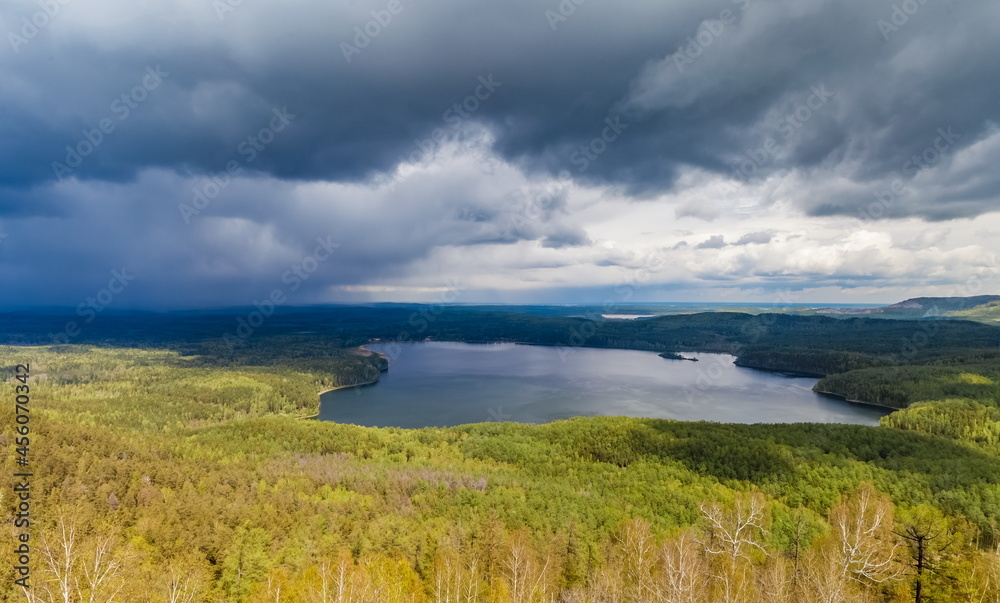 View of the lake from the top of the mountain on the background of mountains, forests, sky with clouds in summer
