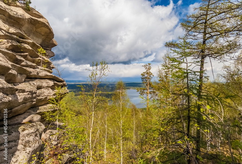 Stone wall, green bushes and trees on the background of the lake, blue sky and white clouds in summer