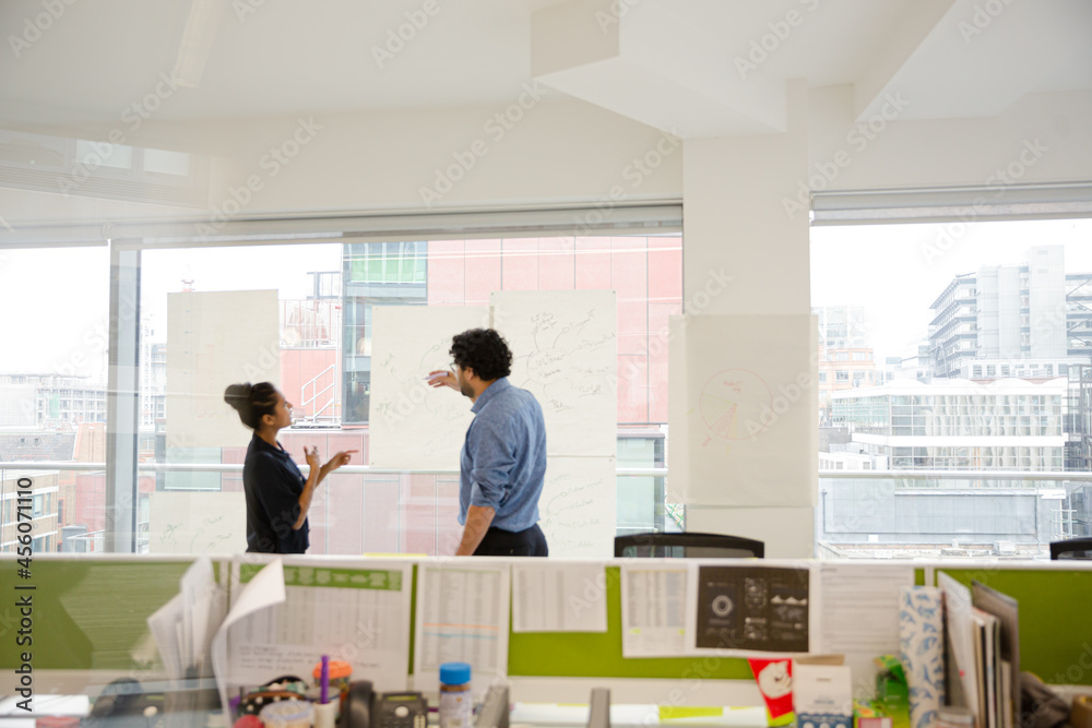 Businessman and businesswoman discussing diagram sketches hanging on conference room window