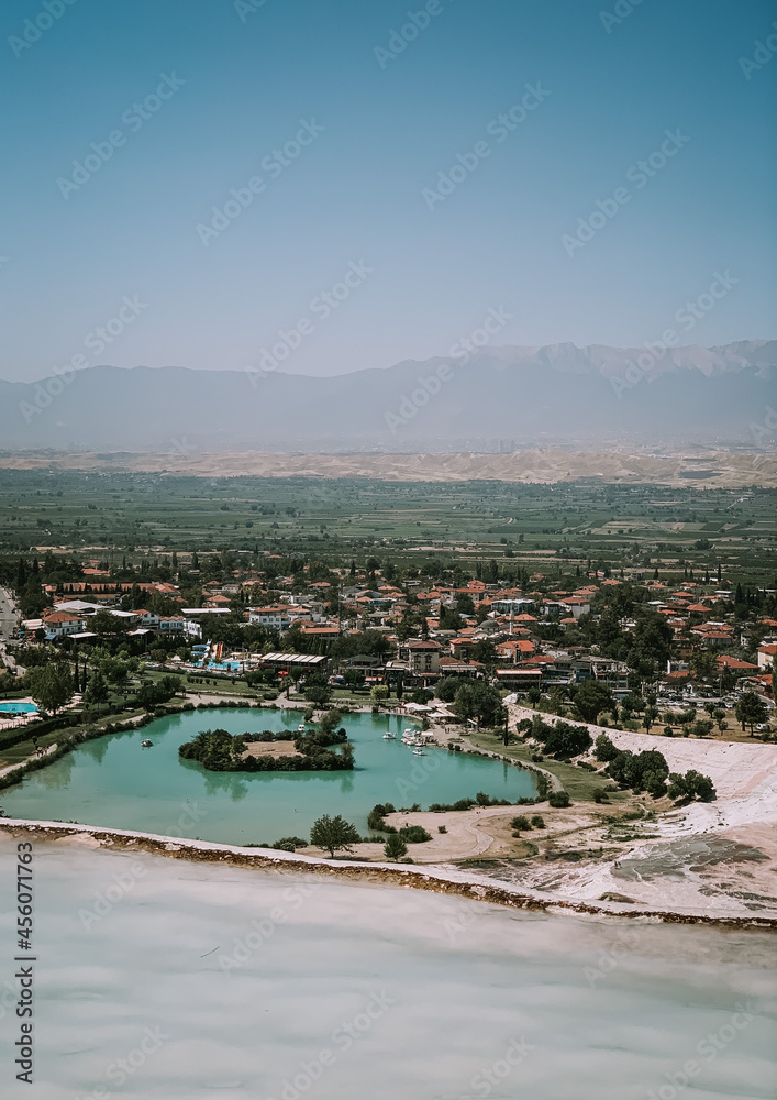 a small southern town with a lake in the center and houses with tiled roofs, mountains in the distance and a light tumanka, in front of a white stone terrace