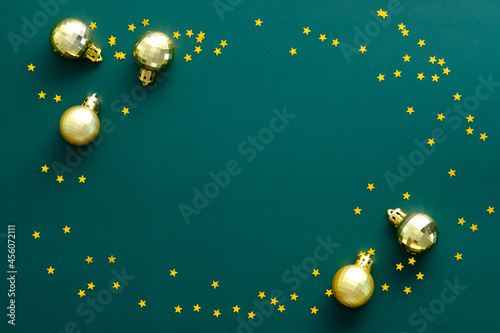 Fototapeta Naklejka Na Ścianę i Meble -  Vintage Christmas frame made of golden balls and confetti stars on green background. Flat lay, top view, overhead.