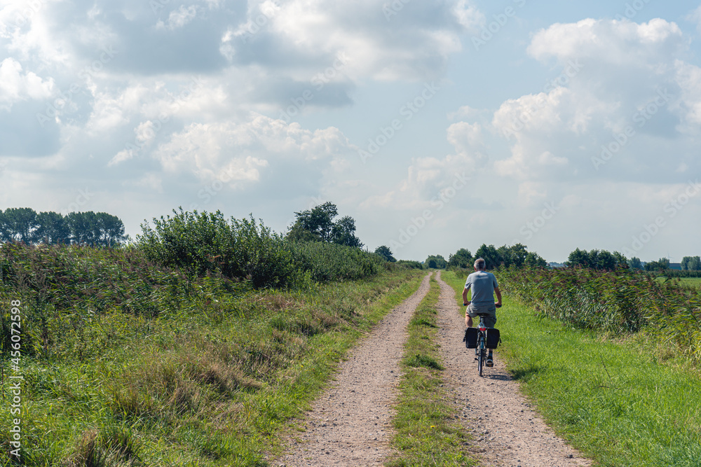 Man in shorts cycles on a sandy path on a seemingly endless long sandy path with parallel wheel tracks in a nature reserve in the Dutch province of North Brabant. It is a sunny summer day.