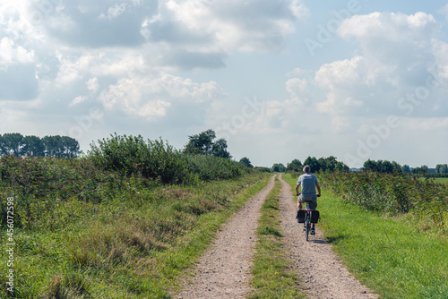 Man in shorts cycles on a sandy path on a seemingly endless long sandy path with parallel wheel tracks in a nature reserve in the Dutch province of North Brabant. It is a sunny summer day.