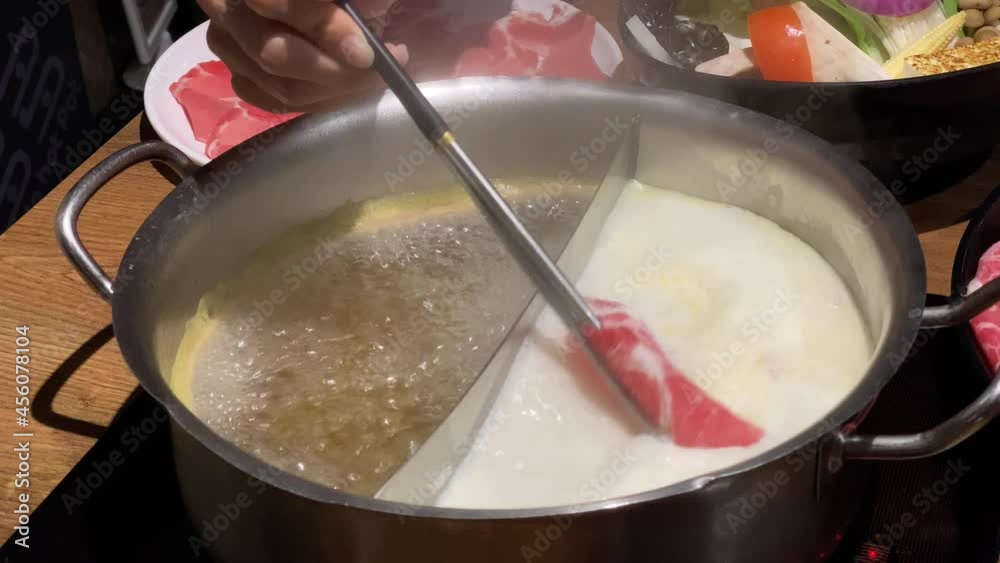 Using chopsticks for cooking a meat in chinese hotpot soup. Plates with fresh and delicious pork and beef raw at a buffet restaurant. Typical hot pot herbal cuisine in Taiwan-Dan Using chopsticks for cooking a meat in chinese hotpot soup. Plates with fresh and delicious pork and beef raw at a buffet restaurant. Typical hot pot herbal cuisine in Taiwan-Dan