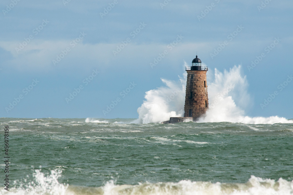 Giant Waves Surround Stone Lighthouse in Maine As Sun Breaks Through Clouds