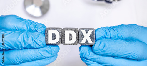 DDX Differential diagnosis - word from stone blocks with letters holding by a doctor's hands in medical protective gloves