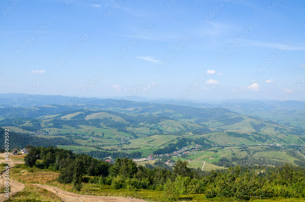 Obraz premium Summer mountain landscape with Pylypets village on the green grassy hills, at the valley, view from Gymba Mountain. Carpathian Mountains, Ukraine