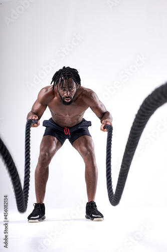 Attractive muscular african man working out with heavy ropes isolated over white studio background. Photo of handsome man with naked torso durign workout. sport, fitness concept. portrait