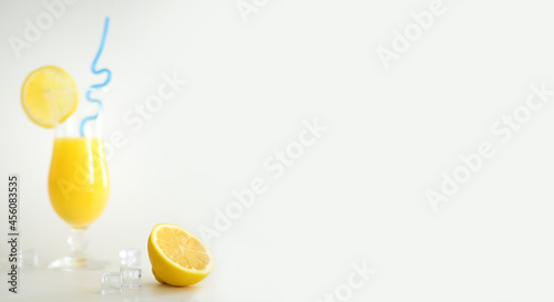 Fresh orange juice in glass  decorated with slice of lemon and blue straw. Summer cocktail on the white background. Colorful template. Free space for text  copy space.