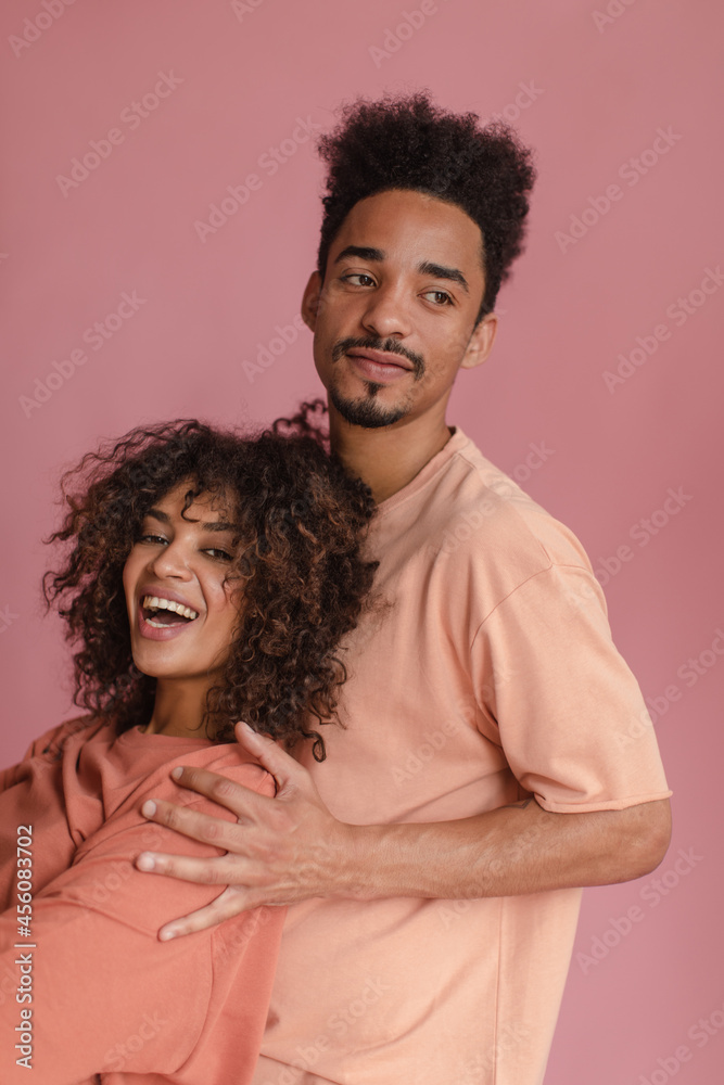 image of lovely couple people of African appearance on isolated pink color. tall man with beautifully shaved beard holds cheerful woman with wide open smile by shoulders. image of lovely couple people of African appearance on isolated pink color. tall man with beautifully shaved beard holds cheerful woman with wide open smile by shoulders.