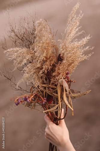 Woman's hand holding a bouquet of dried flowers on a blurred background. Autumn beauty in details