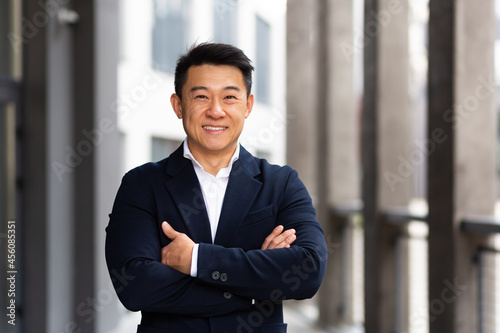 portrait of a cheerful asian in a business suit looks at the camera with crossed arms and smiles