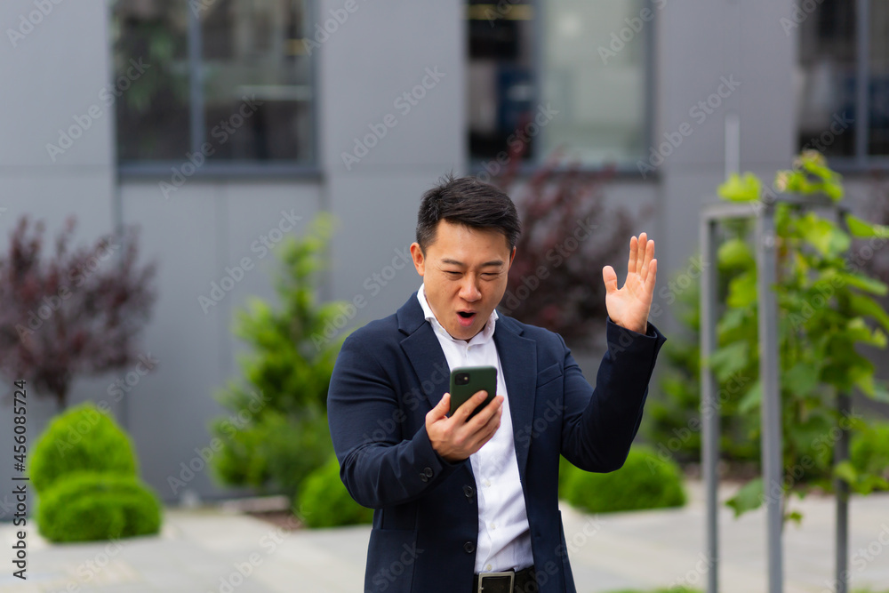 Asian businessman businessman looks at cellphone reads lottery winning news rejoices outside office Asian businessman businessman looks at cellphone reads lottery winning news rejoices outside office