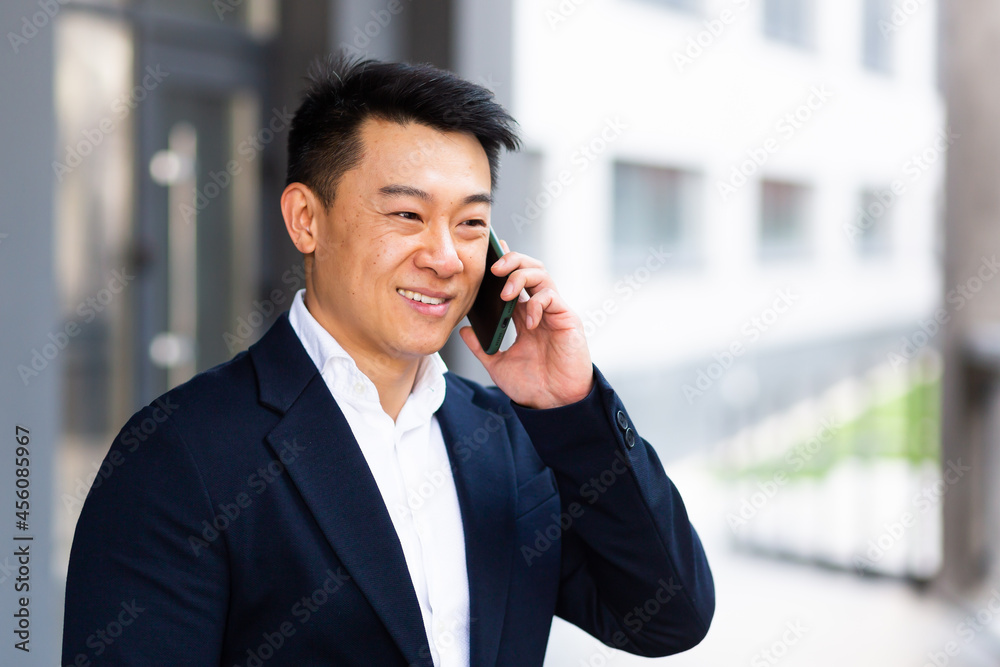 portrait Asian businessman talking on the phone cheerful smiling reports good news near the office center outside looking at the camera portrait Asian businessman talking on the phone cheerful smiling reports good news near the office center outside looking at the camera