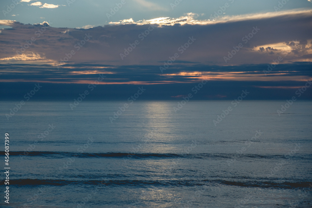 Panoramic view of the pacific ocean and beautiful sunset in the horizon with sun behind clouds and the shore and beach