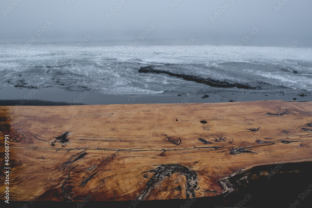 Rustic wood table and panoramic view of the pacific ocean with waves, the horizon with cloudy sky and the shore and beach