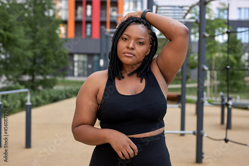 Portrait of confident afro american woman in black tracksuit posing at camera, have rest, black fat lady is looking serious and confident. Sport, healthy lifestyle, workout, fitness concept