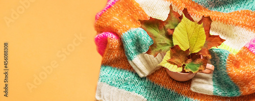 Background with a warm sweater. Knitted clothes with autumn leaves, bright background, knitwear. Autumn-winter concept. Copy space Banner. 