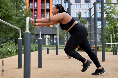 Beautiful african american overweight young woman does fitness outdoors. Fat lady is training on sports ground for weight loss. Sport outside on warm summer day, side view, copy space. sport, workout
