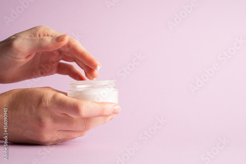 Hand holding cream jar. Hand holding face cream on purple background, close-up. Moisturizer in container. Side view © Nataliia Karabin