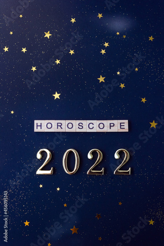 Word Horoscope and 2022 numbers. Wooden blocks with lettering on dark blue background decorated with stars confetti. Vertical flat lay.