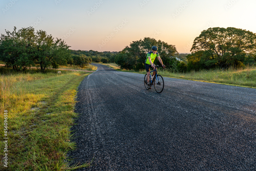 Man, person, rider on a bicycle along a paved road with oak trees and grass, clear sky, Cordillera Ranch, Boerne, Hill Country, Texas