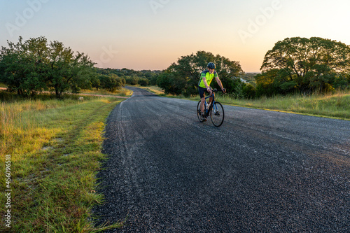 Man, person, rider on a bicycle along a paved road with oak trees and grass, clear sky, Cordillera Ranch, Boerne, Hill Country, Texas