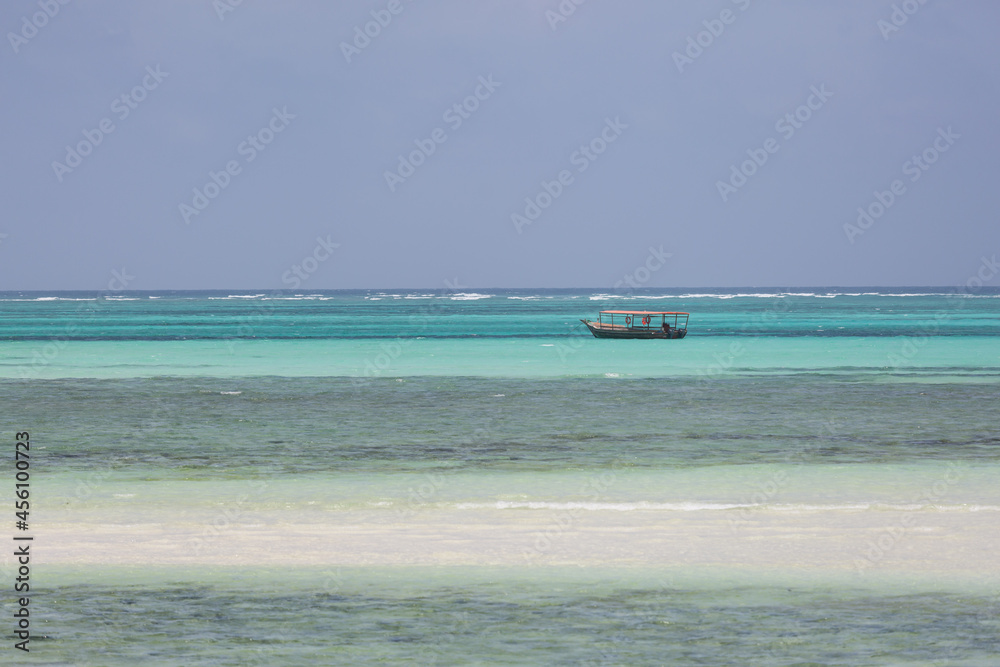 Lonely fishing boat on the endless turquoise ocean with stripes of white sand and karals in the foreground