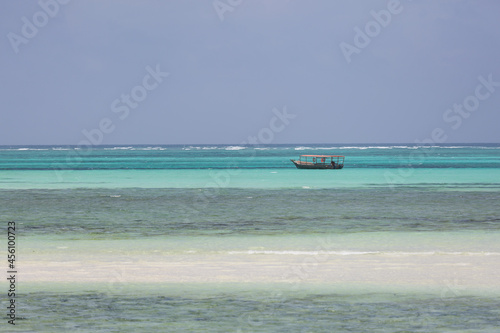 Lonely fishing boat on the endless turquoise ocean with stripes of white sand and karals in the foreground photo